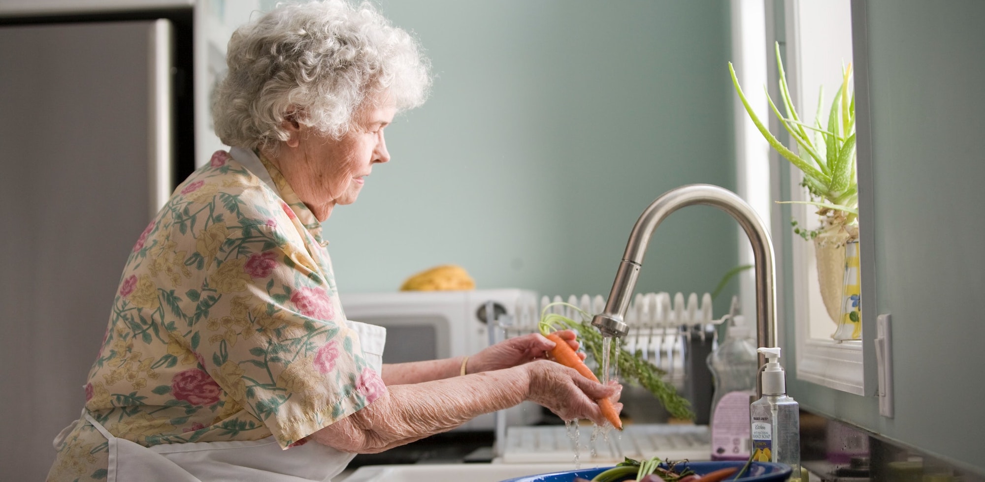 Elderly woman preparing a meal and at sink washing carrots
